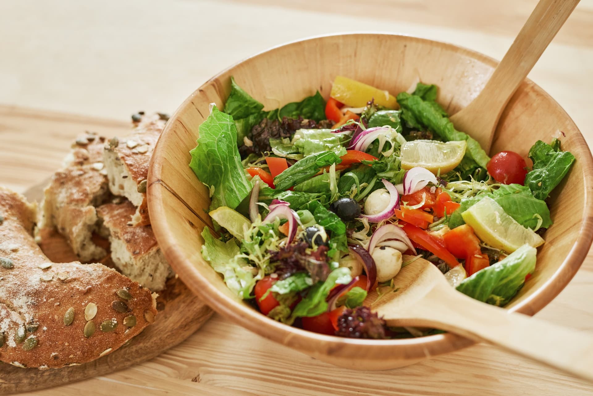 Bowl of fresh mixed salad with tomatoes, red onion and olives beside seeded bread