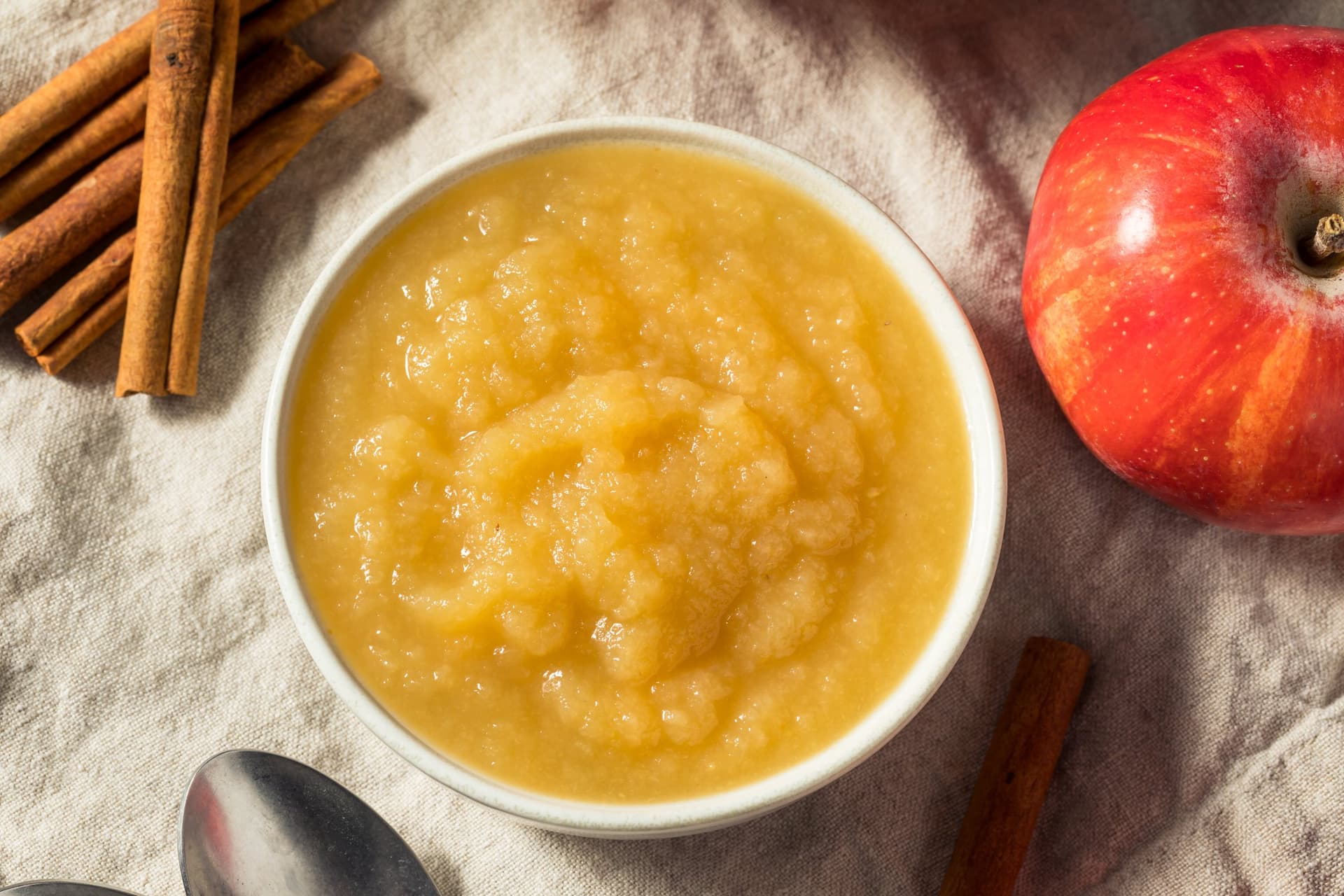 Bowl of apple sauce with cinnamon sticks and a red apple