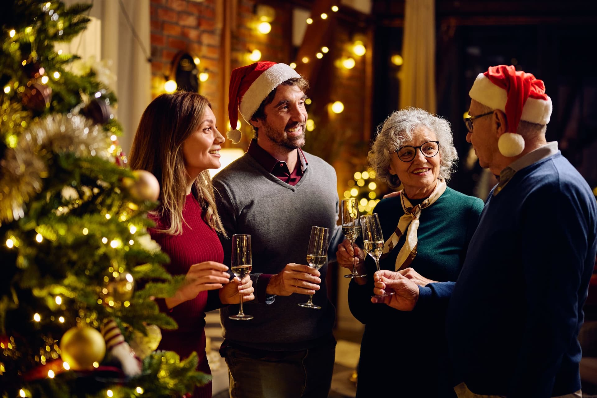 Guests in Santa hats raising a glass by the Christmas tree