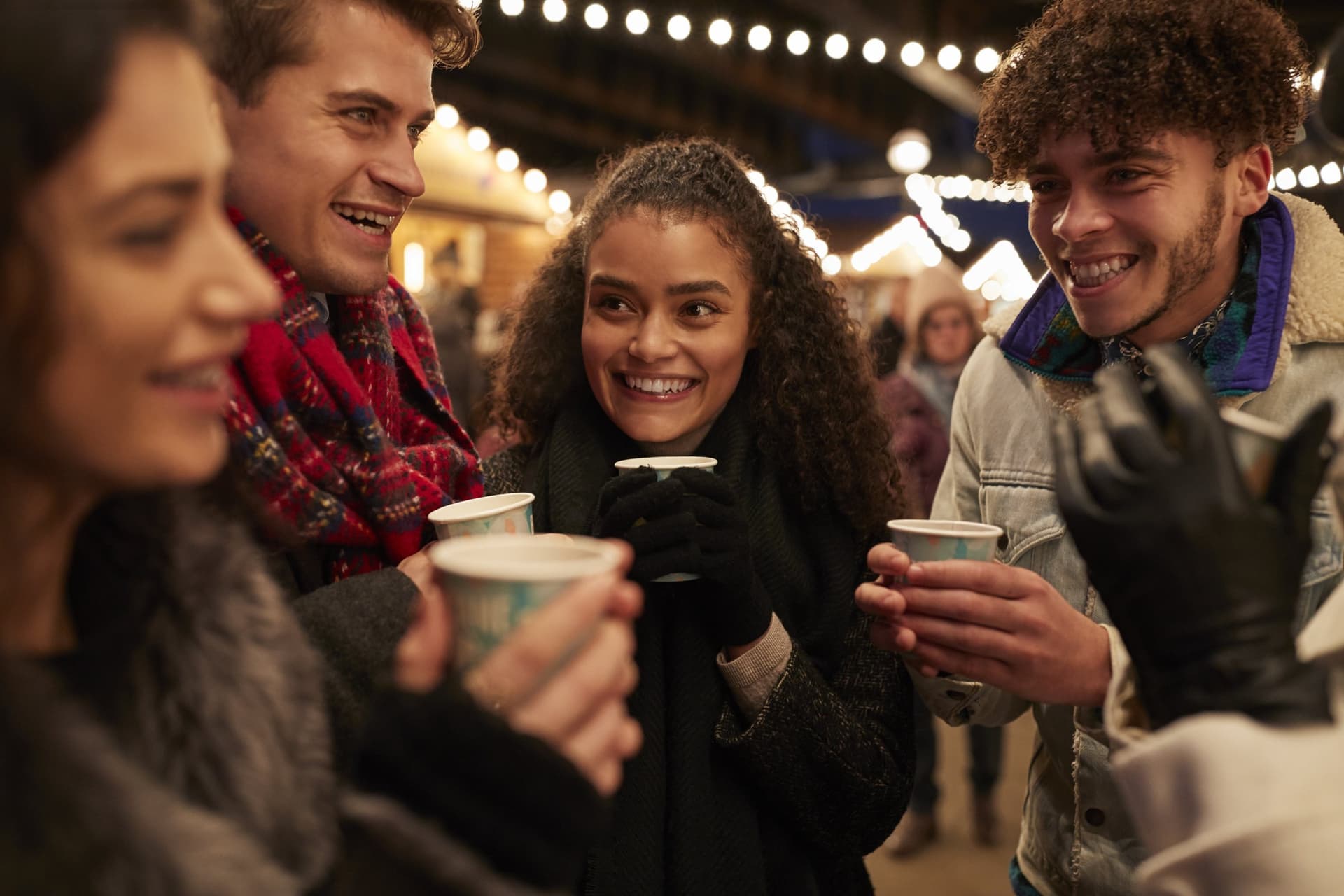 Friends in winter coats with hot drinks at an outdoor Christmas event